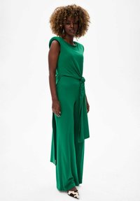 Groene jumpsuit met een knoopdetail in de taille, voorzien van wijde benen en korte mouwen. Glad materiaal met een vloeiende textuur.