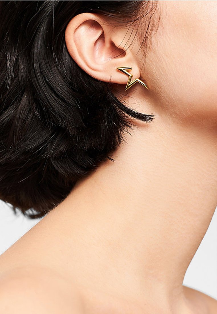 Gouden oorbellen met een zigzagontwerp. De oorbellen hebben een gepolijste afwerking en zijn met een minimalistische achterkant aan het oor bevestigd.