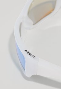 Lunettes de soleil blanches exposées sous un angle, avec des verres teintés d'une teinte bleue dégradée et le logo "ARNETTE" en noir sur le côté.