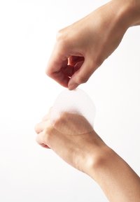 Przezroczysty, teksturowany plasterek uniesiony ręką z nadgarstka. Plastry ma zakrzywiony kształt i lekko klejącą powierzchnię.