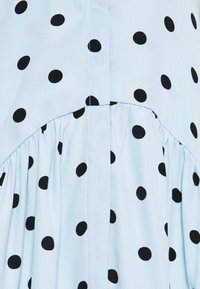 Tissu bleu clair avec des pois noirs. Présente un détail froncé, une couture verticale et une texture lisse. Des éléments de design classiques sont visibles.