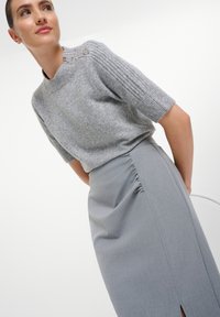 Grauer Wollpullover mit gerippten Ärmeln und drei dekorativen Knöpfen an der Schulter, kombiniert mit einem grauen Bleistiftrock mit seitlicher Raffung.