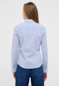 Blue and white striped shirt with long sleeves, button cuffs, and a rounded hem. Tailored fit with a back yoke design. Worn with dark denim.