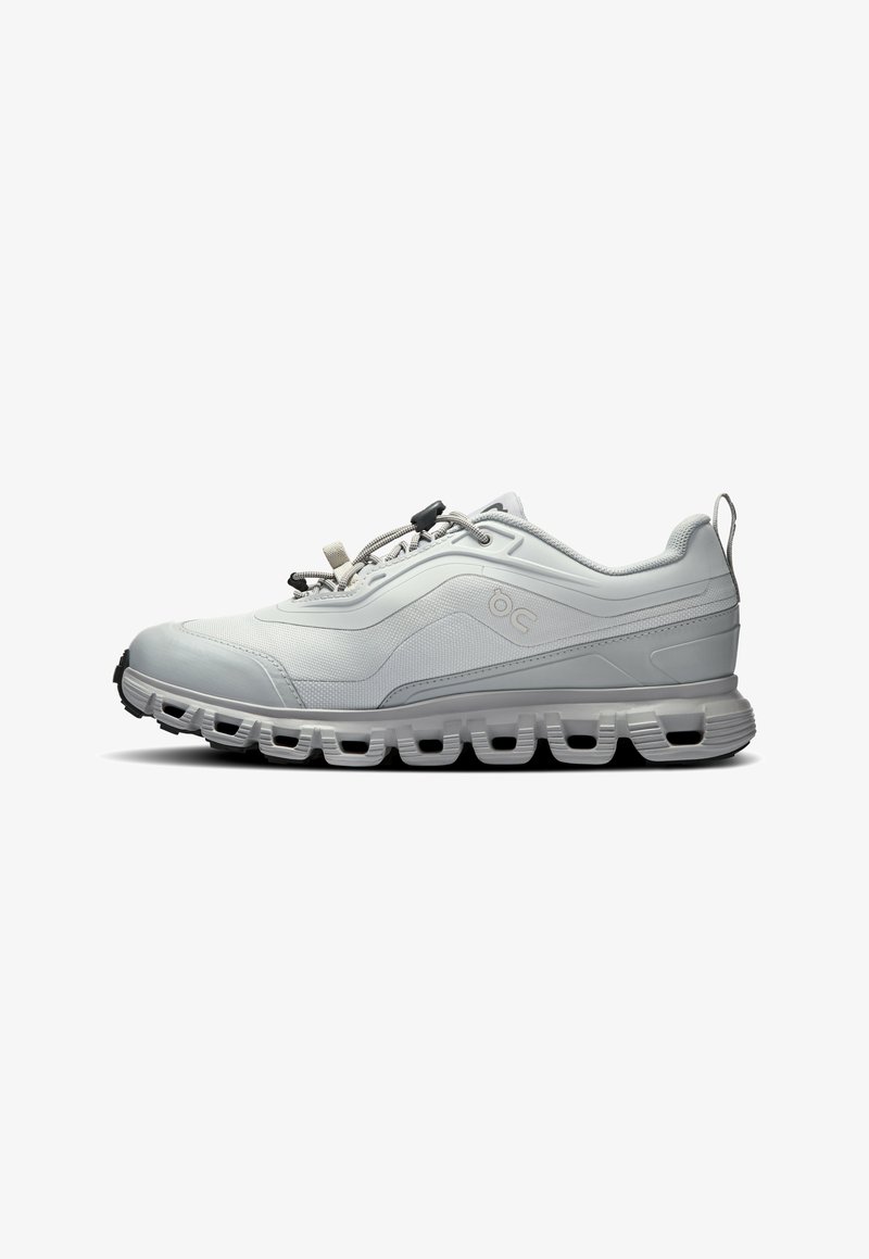 Hellgrauer Sportschuh mit strukturiertem Obermaterial, schlankem Design, abgerundeter Spitze und einer gepolsterten Sohle mit ausgeschnittenen Details. Verstellbare Schnürsenkel inklusive.