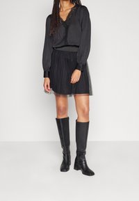 Blouse noire à manches longues avec bordure en dentelle, associée à une jupe en tulle noire et des bottes noires en cuir à talons jusqu'aux genoux. Design simple avec une coupe décontractée.