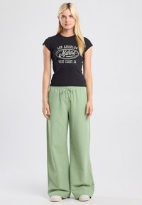 Black short-sleeve t-shirt with white text graphic, paired with green checkered wide-leg pants. Casual cotton blend fabric.