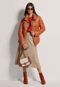 Gevoerde oranje jas met zwarte hardware, rode gebreide trui, beige midi rok en bruine suède enkellaarsjes. Witte handtas met tan accenten.