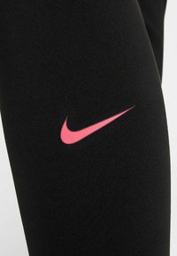 Leggings de sport noirs en tissu extensible avec un logo Nike rose bien visible sur le côté gauche inférieur. Texture lisse, design ajusté.