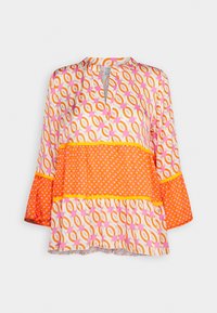 Blouse à manches longues avec motifs géométriques et pois orange, rose et blancs, col en V et coupe ample, présentée sur fond blanc.