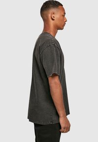 T-shirt oversize gris foncé avec manches courtes, col rond et coutures usées pour un look décontracté, accompagné de pantalons noirs.
