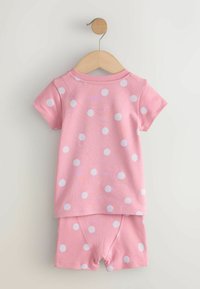 Ensemble pour tout-petit à manches courtes rose avec des pois blancs, comprenant un haut et un short, suspendu à un cintre en bois sur un fond blanc.