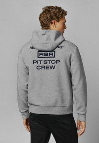 Šedá mikina s kapucňou, na zadnej strane s nápisom "RBR PIT STOP CREW" tmavomodrou farbou. Zmes bavlny, rebrované manžety a lem.