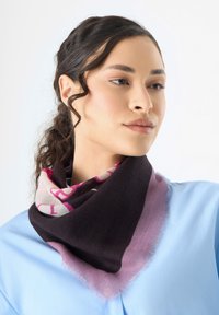 Écharpe triangulaire en noir, rose et crème, avec un motif. Le tissu a une texture douce avec des bords effilochés. Portée autour du cou.