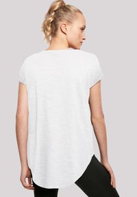 Short-sleeve, white t-shirt featuring a relaxed fit and curved hem. Fabric appears soft with a subtle texture. Worn with black leggings.