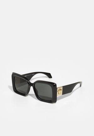 Óculos de sol quadrados pretos com lentes coloridas e acabamento brilhante. Apresenta detalhes em dourado com um emblema decorativo de leão nas hastes.