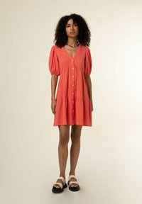 Koralle farbenes Hemdkleid mit Puffärmeln und geschichtetem Rüschensaum. Aus strukturiertem Stoff gefertigt, mit einem V-Ausschnitt und vorderen Knöpfen.
