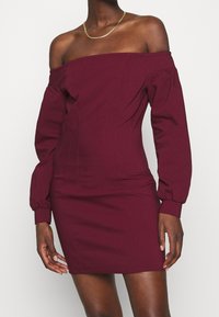 Bordeauxfarbene schulterfreie Kleid mit langen Puffärmeln, figurbetontem Schnitt, strukturierten Nähten und glatter Stofftextur. Mit Mini-Länge.