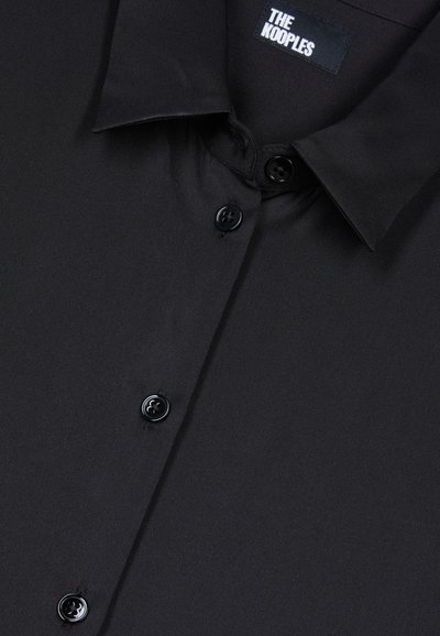 Camicia nera con bottoni, realizzata in tessuto liscio, colletto a punta e cinque bottoni neri. L'etichetta recita "THE KOOPLES."