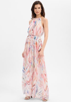 Frau trägt ein ärmelloses, bodenlanges Kleid mit mehrfarbigem abstraktem Muster und Taillierung, steht vor einem schlichten weißen Hintergrund.