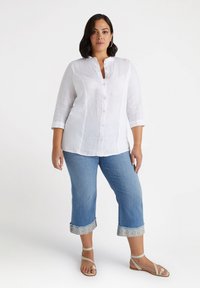 Camisa de lino blanca con botones, con cuello y mangas tres cuartos, combinada con unos jeans recortados de color azul claro que tienen puños con estampado.