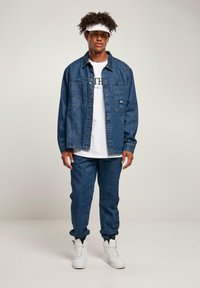 Denim jaka ar divām priekšējām kabatām, apvienota ar baltu T-kreklu ar melnu tekstu. Pieguļošas denim bikses un baltas kedas noslēdz izskatu.