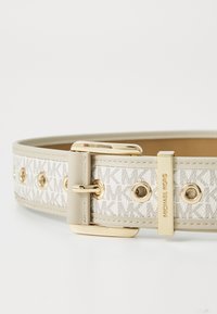 Cintura in pelle tan con un centro in tessuto beige chiaro caratterizzato da un motivo ripetuto. La design è completata da accessori in tono oro e accenti circolari.