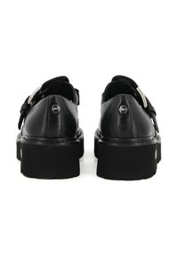 Scarpe in cuoio nero con punta tonda, dotate di una cintura con fibbia e suola spessa a righe. La vista posteriore mostra dettagli in metallo.