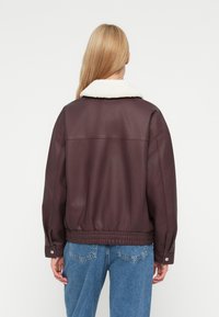 Giacca in pelle burgundy con colletto in pelliccia bianca, vita elastica e polsini con bottoni, vista da dietro. Materiale testurizzato e design informale.