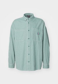 Long-sleeve button-up shirt with vertical green and white stripes, two chest pockets, and a small logo on the right pocket.