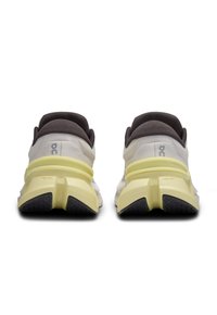 Baskets de sport blanches et jaune clair avec une tige texturée, des accents marron foncé, une semelle épaisse et une semelle en caoutchouc noir à motif.