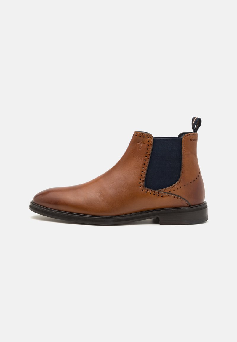 Botín Chelsea de cuero marrón con paneles laterales elásticos en color navy, puntera redonda, detalles perforados y suela de goma negra. Tirador trasero para facilitar su colocación.