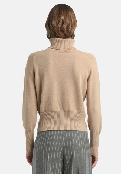 Šviesiai smėlinės spalvos turtleneck megztinis iš minkštos mezginio medžiagos su įmaukščių ir apatinio krašto raukšlėmis, derinamas su pilkais juostelėmis dekoruotais kelnėmis.