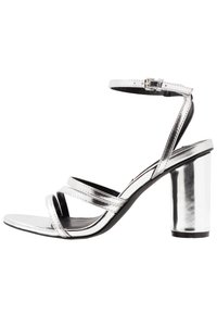 Srebrne metaliczne sandały na wysokim obcasie z grubym obcasem, z trzema równoległymi paskami z przodu i paskiem na kostkę z klamerką.
