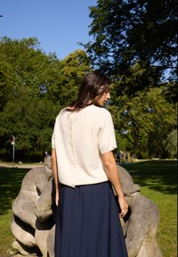 Light beige short-sleeve sweater features a textured finish and a row of buttons at the back, paired with a flowing navy skirt.