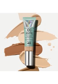 Tube de crème CC+ Natural Matte d'IT Cosmetics avec SPF 40 sur un fond aux nuances de maquillage étalées beige, bronzé et marron.