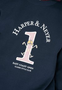 Felpa blu navy con collo a giro. Presenta testo bianco e un grande design a strisce con il numero uno, accentuato da mazze da golf incrociate e un cappellino.