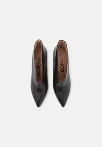 Black leather pointed-toe shoes with a sleek design, featuring a smooth texture and minimalistic slip-on style. Accented with a brown insole.