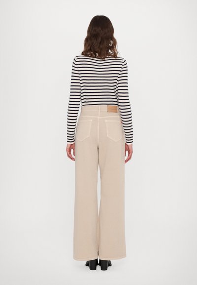 Beige wijde broek met een hoge taille, voorzien van een vierkante achterzak en een tan leren label. Gecombineerd met een zwart-wit gestreepte top.