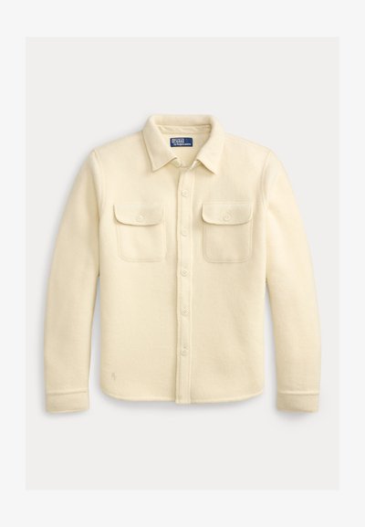 Dlhá vlnená košeľa v krémovej farbe s gombíkmi na zapínanie na prednej strane, dvoma prednými vreckami s chlopňami a golierom, značka Polo Ralph Lauren vo vnútri goliera.