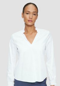 Weiße Bluse mit langen Ärmeln, einem Rüschenausschnitt und V-Ausschnitt. Weicher, glatter Stoff mit lockerer Passform und elastischen Bündchen.