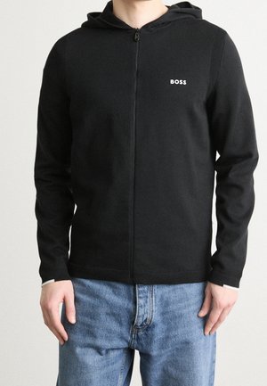 Felpa nera con zip realizzata in tessuto morbido, caratterizzata da una texture a costine sulle spalle, un piccolo logo bianco e polsini a contrasto.