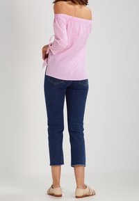 Růžovo-bílý pruhovaný top s odhalenými rameny a zavazovacími detaily na rukávech, doplněný tmavě modrými zkrácenými džíny a béžovými plochými botami.