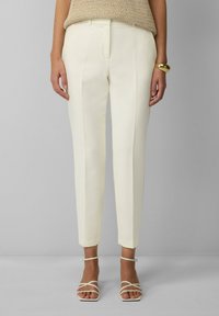 Witte op maat gemaakte broek met een slim fit, voorzien van scherpe plooien en gezoomde manchetten. Gecombineerd met lichte, bandjes sandalen.