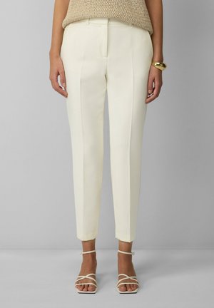 Pantalons blancs ajustés avec une coupe slim, comportant des plis nets et des ourlets. Associés à des sandales légères à lanières.