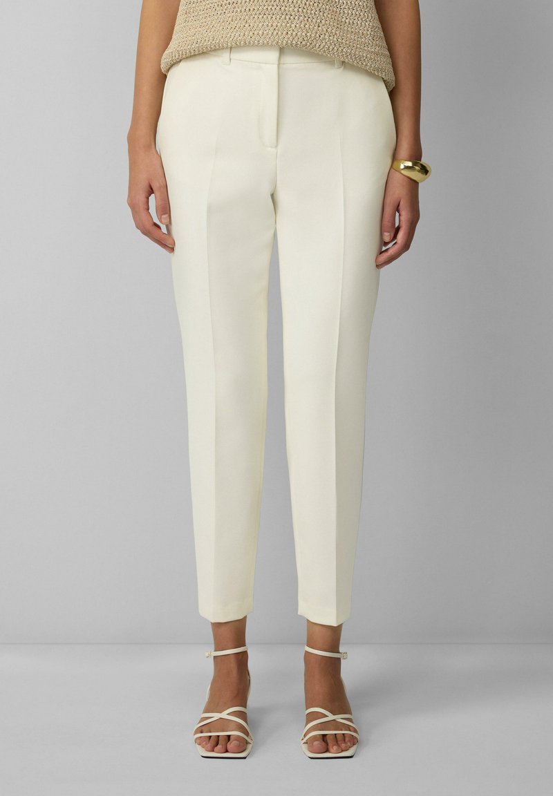 Witte op maat gemaakte broek met een slim fit, voorzien van scherpe plooien en gezoomde manchetten. Gecombineerd met lichte, bandjes sandalen.