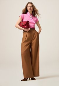 Top rosa aderente con scollatura decorata, pantaloni a vita alta beige a gamba larga e una borsa rossa. Tacchi con stampa animale completano il look.