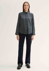 Striped, long-sleeve shirt in dark blue with light accents, button-up front, and a classic collar. Paired with dark blue high-waisted pants.