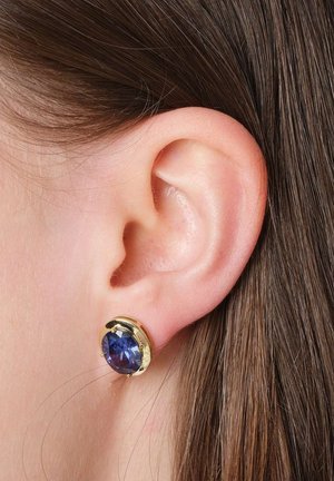 Close-up of a person's ear with brown hair wearing a gold stud earring set with a large round blue gemstone.