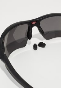 Czarne okulary przeciwsłoneczne z szarymi szkłami, wyposażone w gumowe poduszki na nos i zdejmowane czarne wkładki na uszy, uzupełniające smukły, sportowy design.