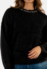 Suéter negro esponjoso con un escote redondo, decorado con cuentas plateadas en el cuello. Mangas largas, textura suave y un ajuste relajado.